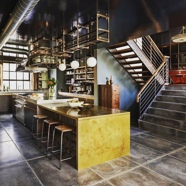 Kitchen with brass-finish island, bar stools, open steel shelving and floating staircase