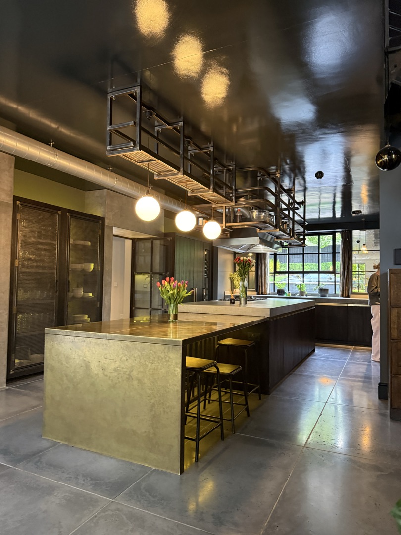 The Ponds Goostrey — brass kitchen island with tulips, suspended steel pot rack and Crittall window beyond