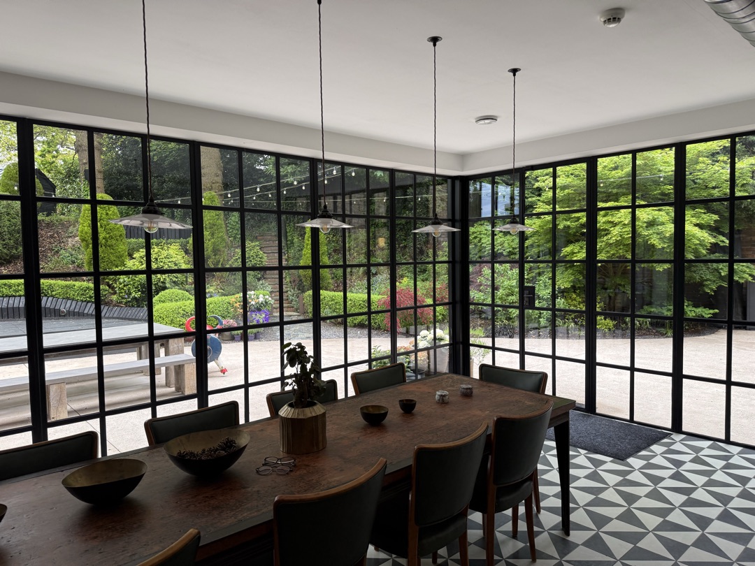 The Ponds Goostrey — dining table set under industrial pendant lights with full-height Crittall glazing