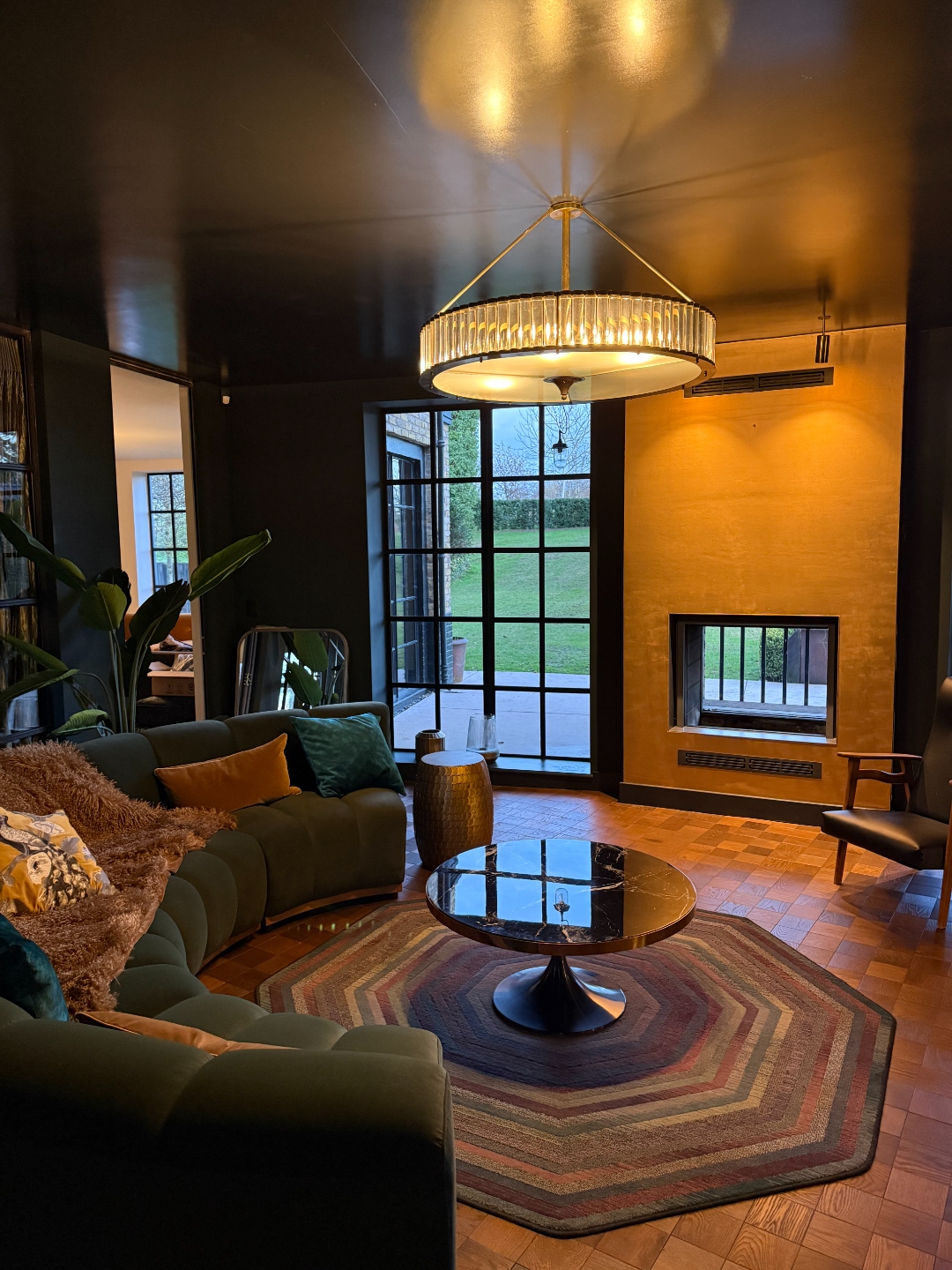 Lounge with green velvet curved sofa, art deco chandelier, gold-leaf fireplace and Crittall garden doors