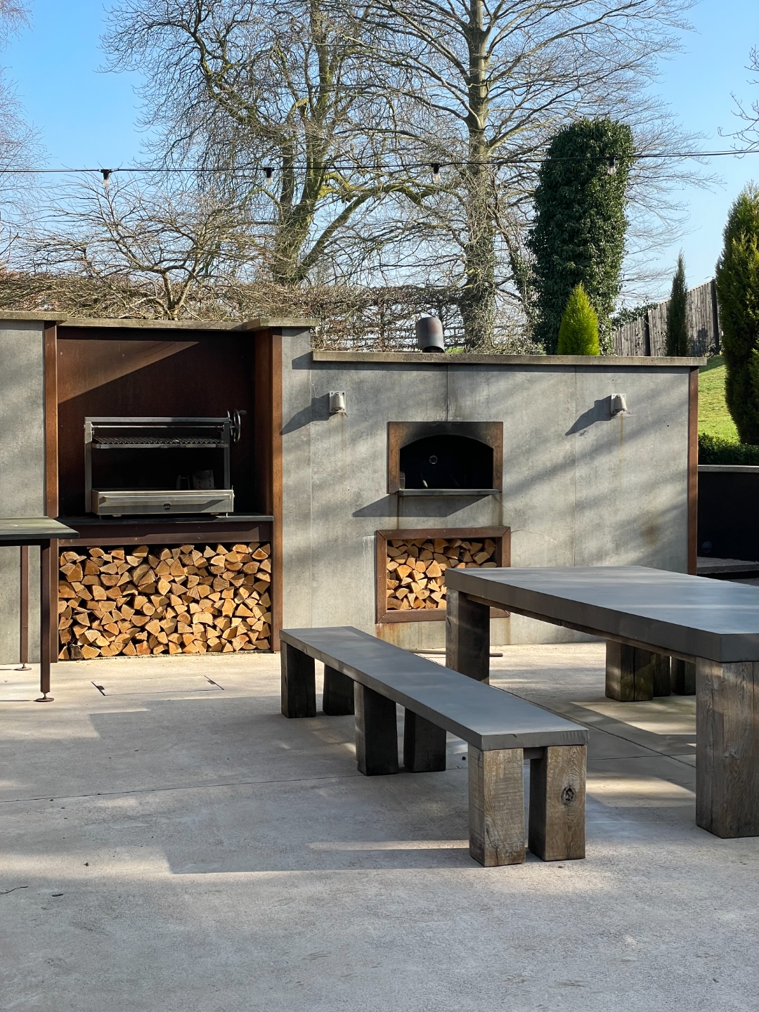 Outdoor kitchen with BBQ grill, pizza oven, log storage and oak bench