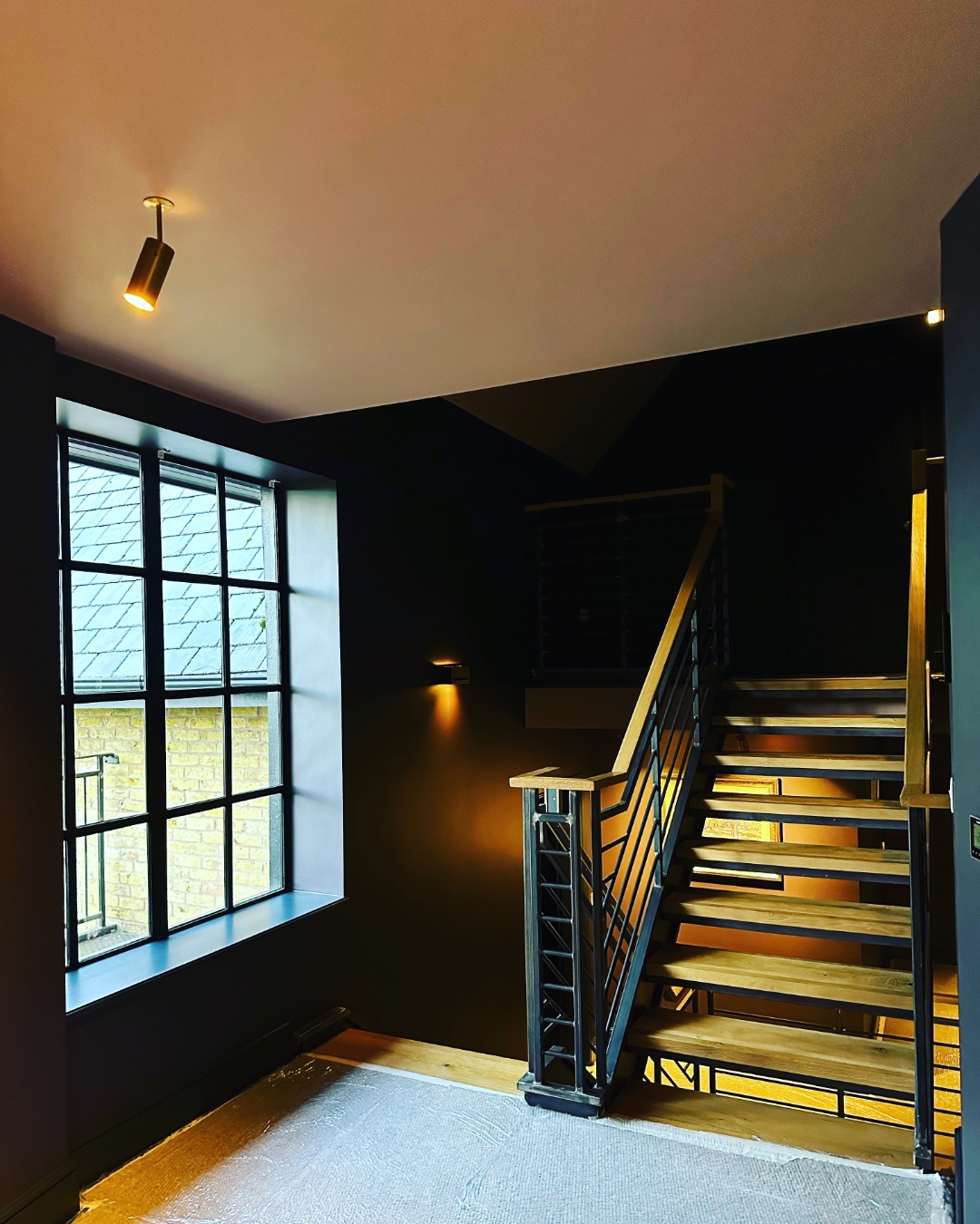 Dark stairwell with Crittall window, oak treads and steel balustrading